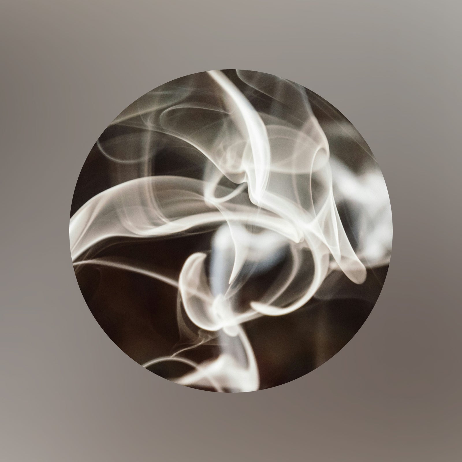 Ein kreisförmiges Bild zeigt wirbelnde weiße Rauchmuster vor einem dunklen Hintergrund, die abstrakte, fließende Formen bilden. Die Ränder des Kreises gehen sanft in einen gräulichen Farbverlauf über.