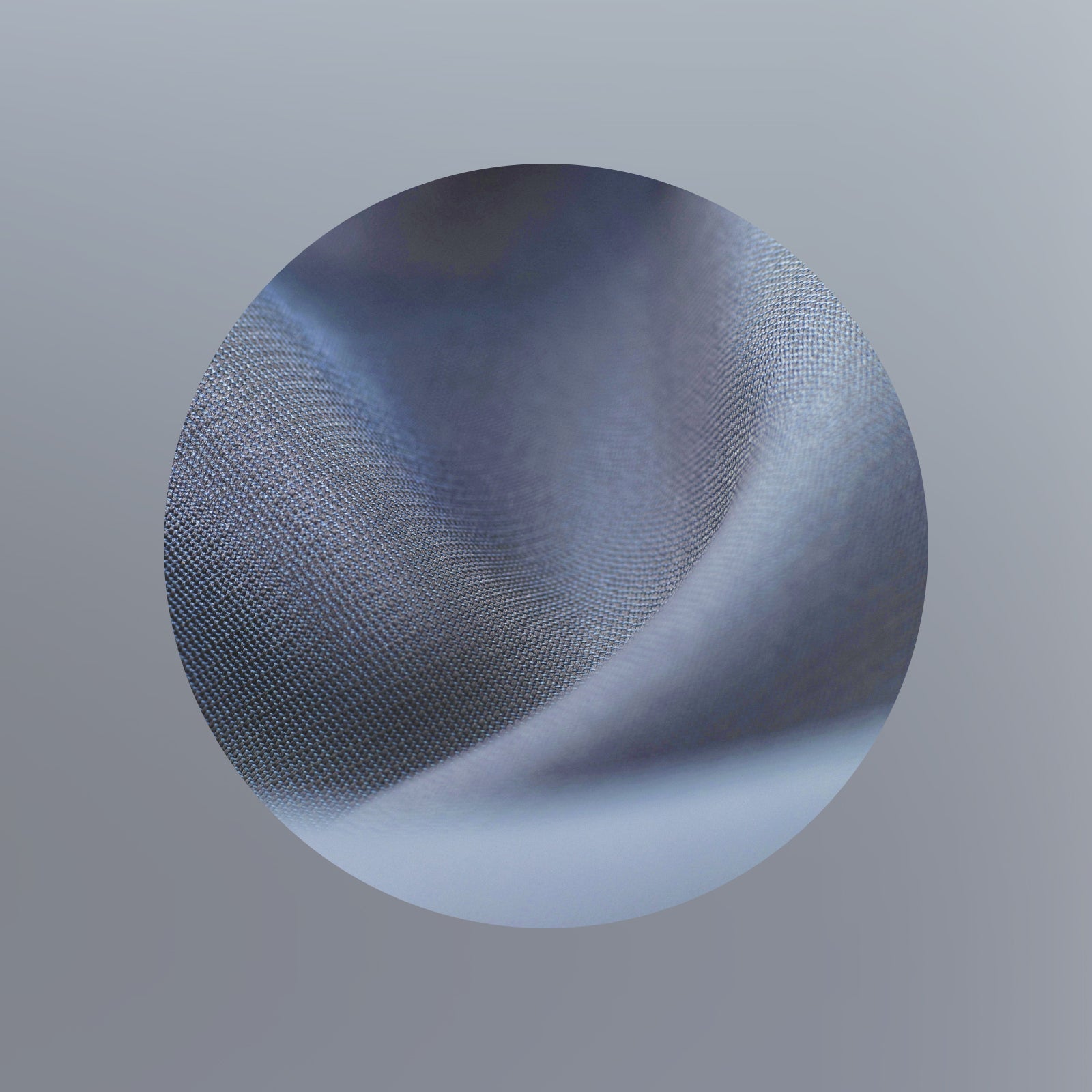Eine Nahaufnahme eines weichen, blaugrauen Stoffes mit sichtbarer Textur und sanften Falten, dargestellt in einem kreisförmigen Rahmen auf einem glatten, grauen Hintergrund mit Farbverlauf.